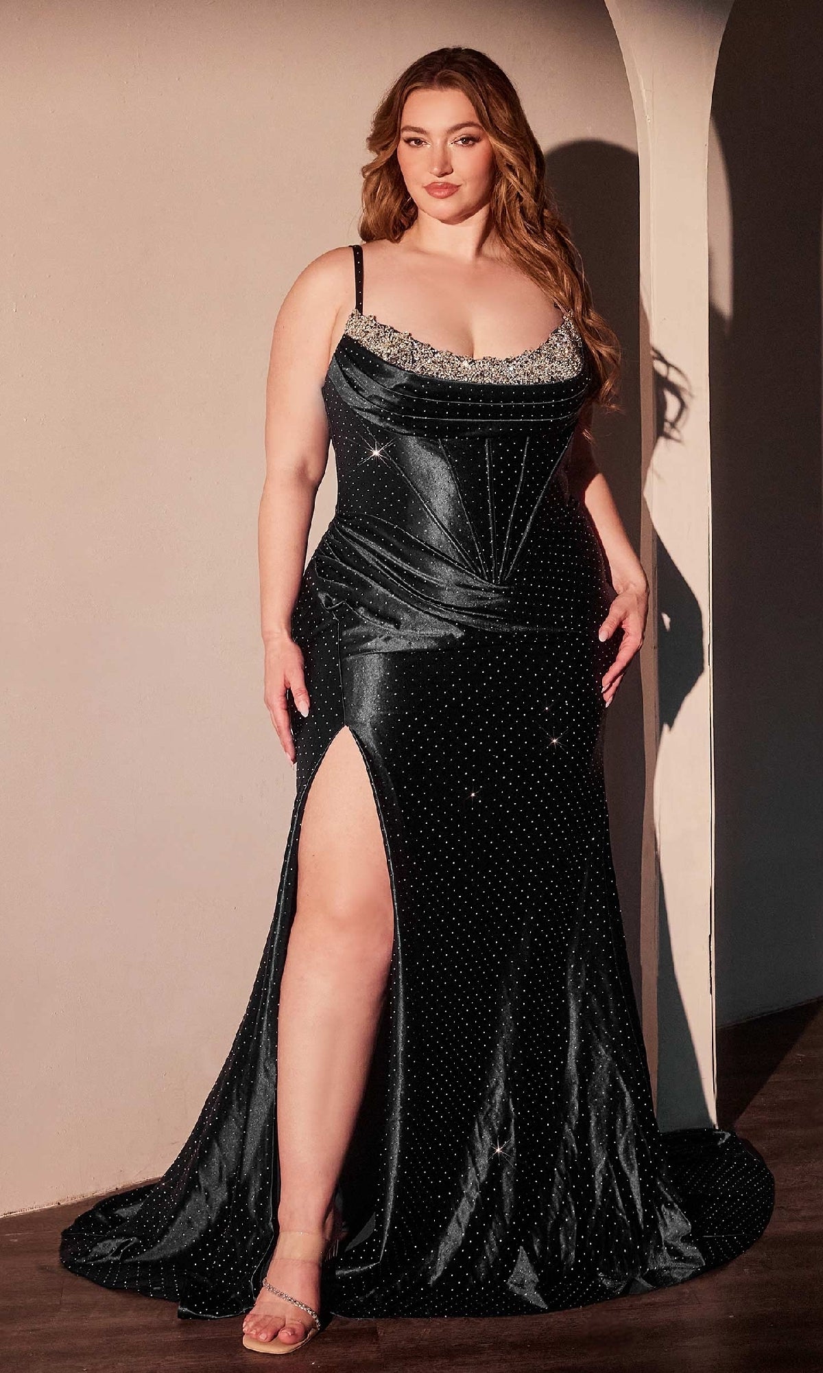 A woman poses against a neutral wall wearing the Ladivine CDS529C, a plus-size long satin prom dress featuring a thigh-high slit and silver embellishments.