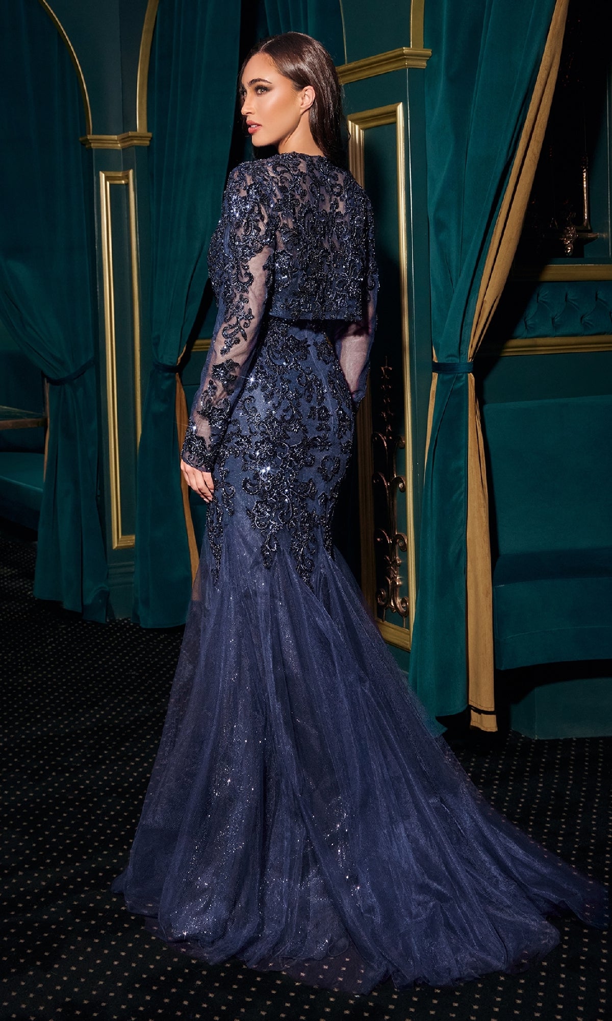 Woman in a dark blue sequined gown standing in an opulent room with green curtains and gold accents.