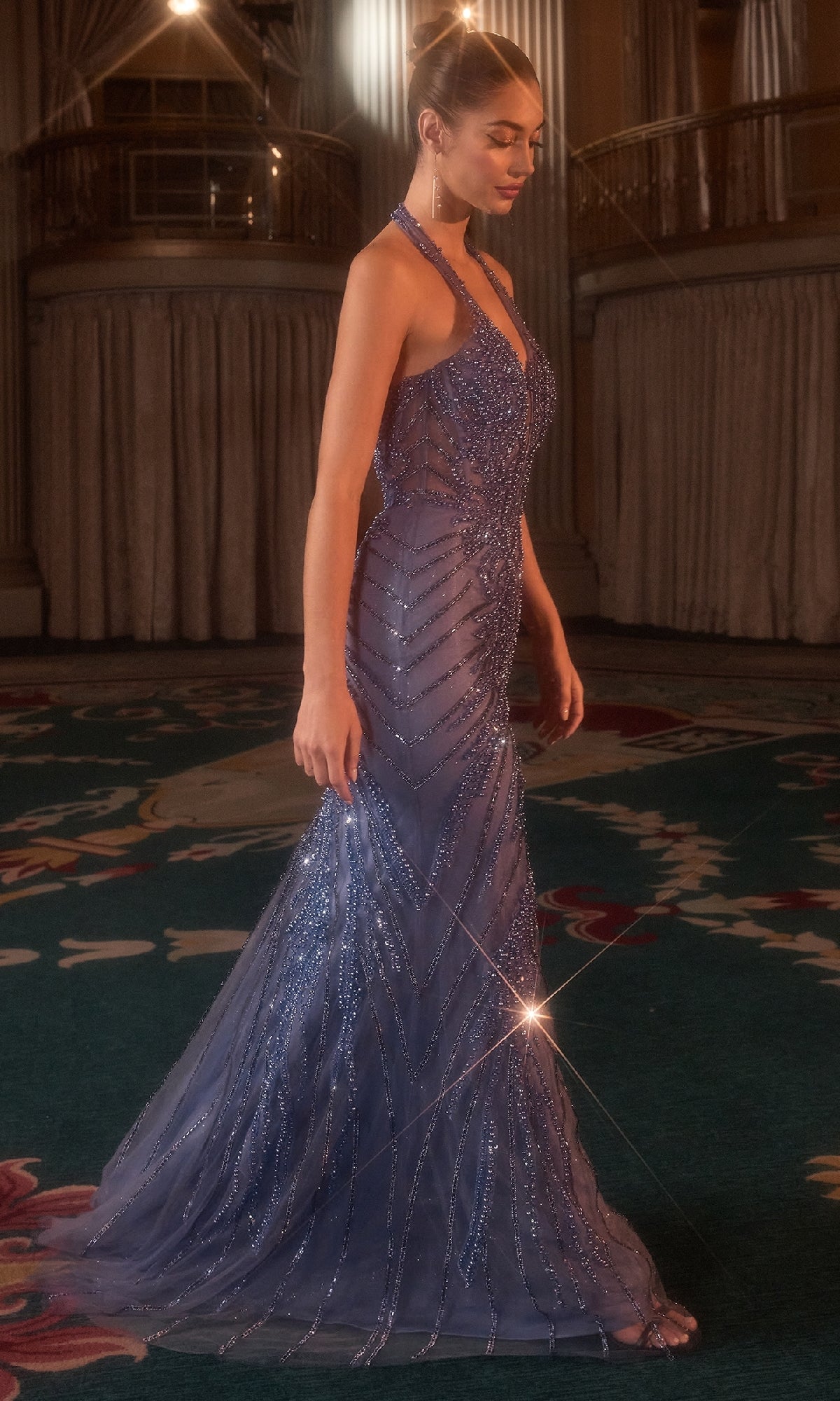 Woman in a sparkling blue evening gown standing on a patterned carpet.
