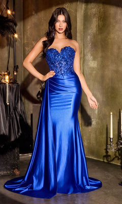 A woman stands indoors against a textured wall, wearing the Ladivine CDS565 Long Prom Dress—strapless, royal blue satin with floral embellishments and a beaded sheer panel on the bodice.