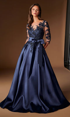 A woman is wearing the Ladivine CDS569 Long Formal Dress, a floor-length navy blue evening gown featuring embroidered lace detailing on the bodice and sleeves, and a large satin bow at the waist, as she stands against a plain brown background.
