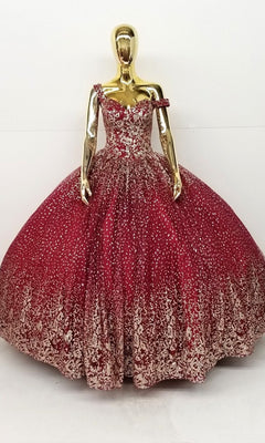 A gold mannequin displays the Quinceanera Dress CHF3001 by Chicas, featuring an off-shoulder, sparkling burgundy ball gown with a voluminous skirt and intricate metallic embroidery, set against a plain white background.