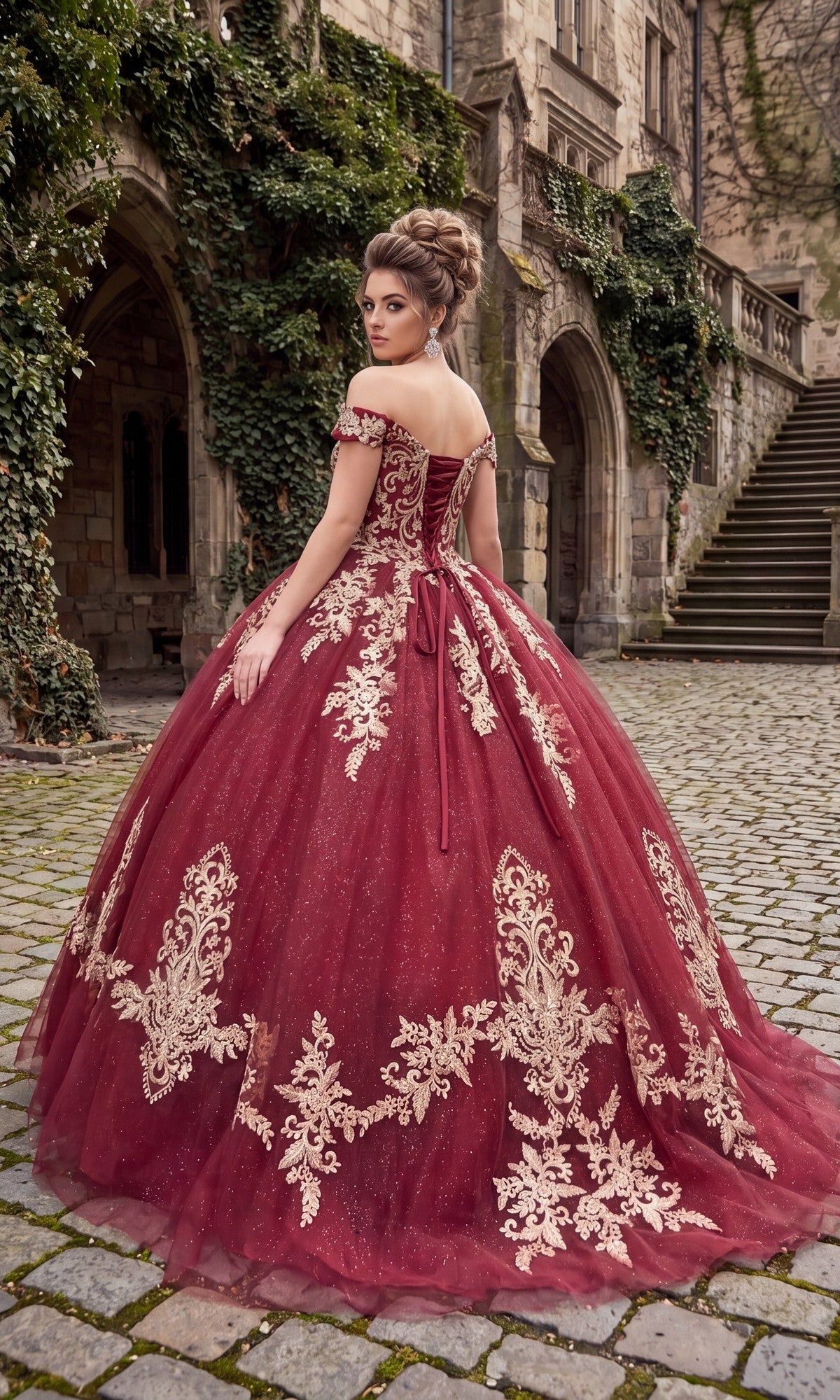 A woman wearing the Quinceanera Dress CHF3008 By Chicas—a burgundy off-the-shoulder gown with gold embroidery—stands on a cobblestone path near an old stone building covered in ivy.
