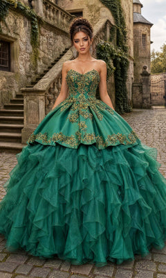 A woman stands in a cobblestone courtyard near a stone building and staircase, wearing the Quinceanera Dress CHF3009 By Chicas in striking Green/Gold. The elaborate gown features a luxurious satin strapless bodice with gold embroidery and a dramatic ruffled organza skirt, enhancing the opulent scene.