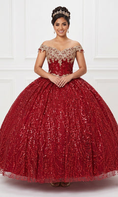 A young woman wearing the Quinceanera Dress CHF3011 By Chicas in burgundy, featuring an ornate off-the-shoulder design and corset back, with a tiara on her head, stands with hands clasped in front of a white decorative wall.