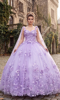 A woman in the lilac Quinceanera Dress CHF3018 by Chicas, featuring an off-shoulder design and delicate floral appliqués, stands on a cobblestone path before an old ivy-covered stone building, with the graceful two-piece cape draping elegantly behind her.
