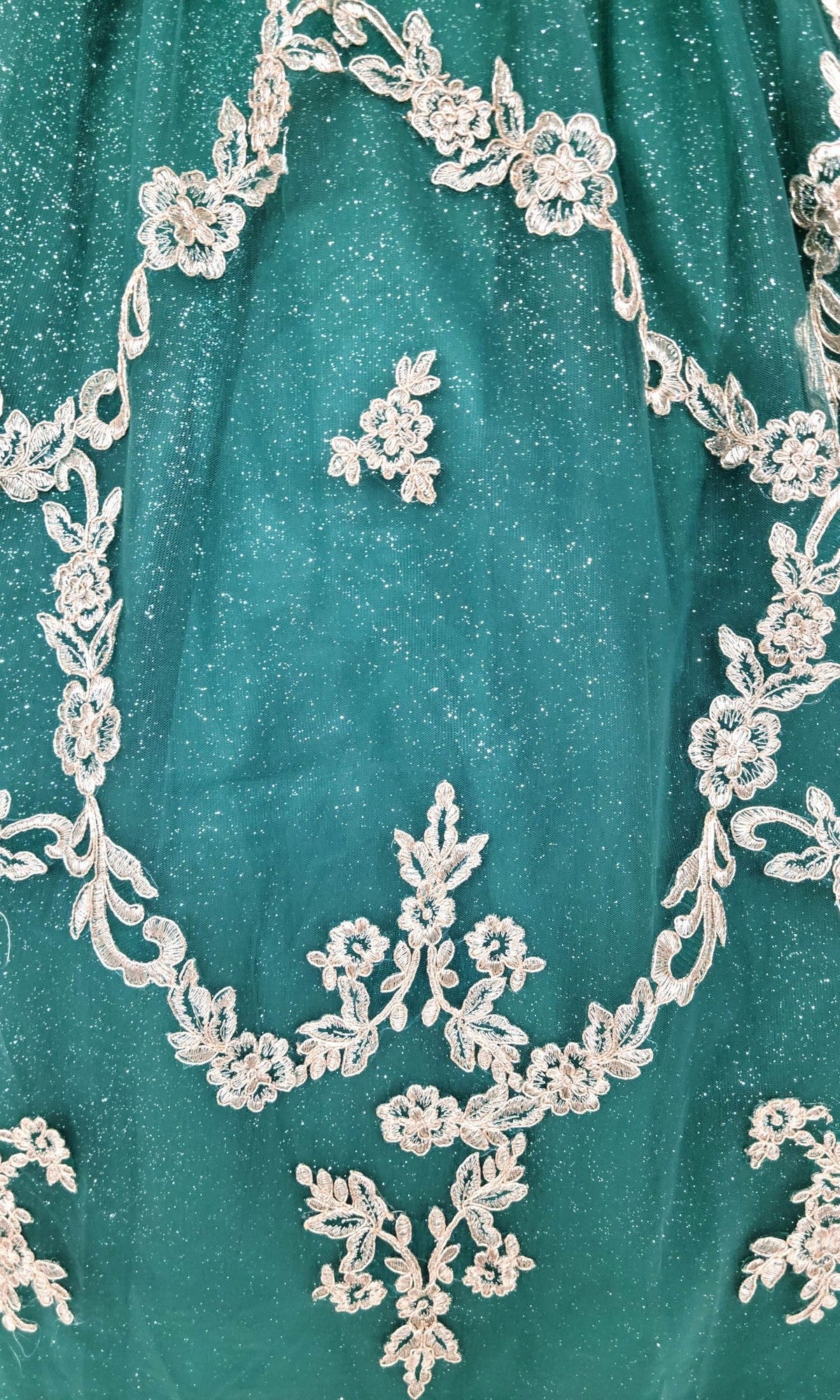 Quinceanera Dress CHF3025 By Chicas: A green fabric enhanced with silver floral embroidery and shimmer, showcasing an ornate circular floral motif at the center—evoking the elegance of a glitter-tulle ballgown designed for special occasions.