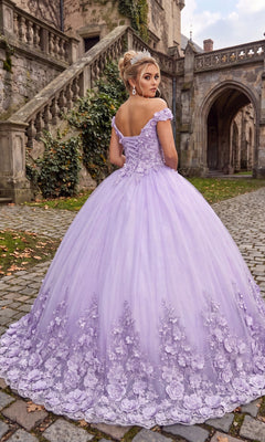 Wearing the Quinceanera Dress CHF3030 by Chicas—a lavender tulle ballgown adorned with delicate 3D floral accents—a woman stands on a stone path beside an old building draped in ivy and featuring graceful arched entryways.