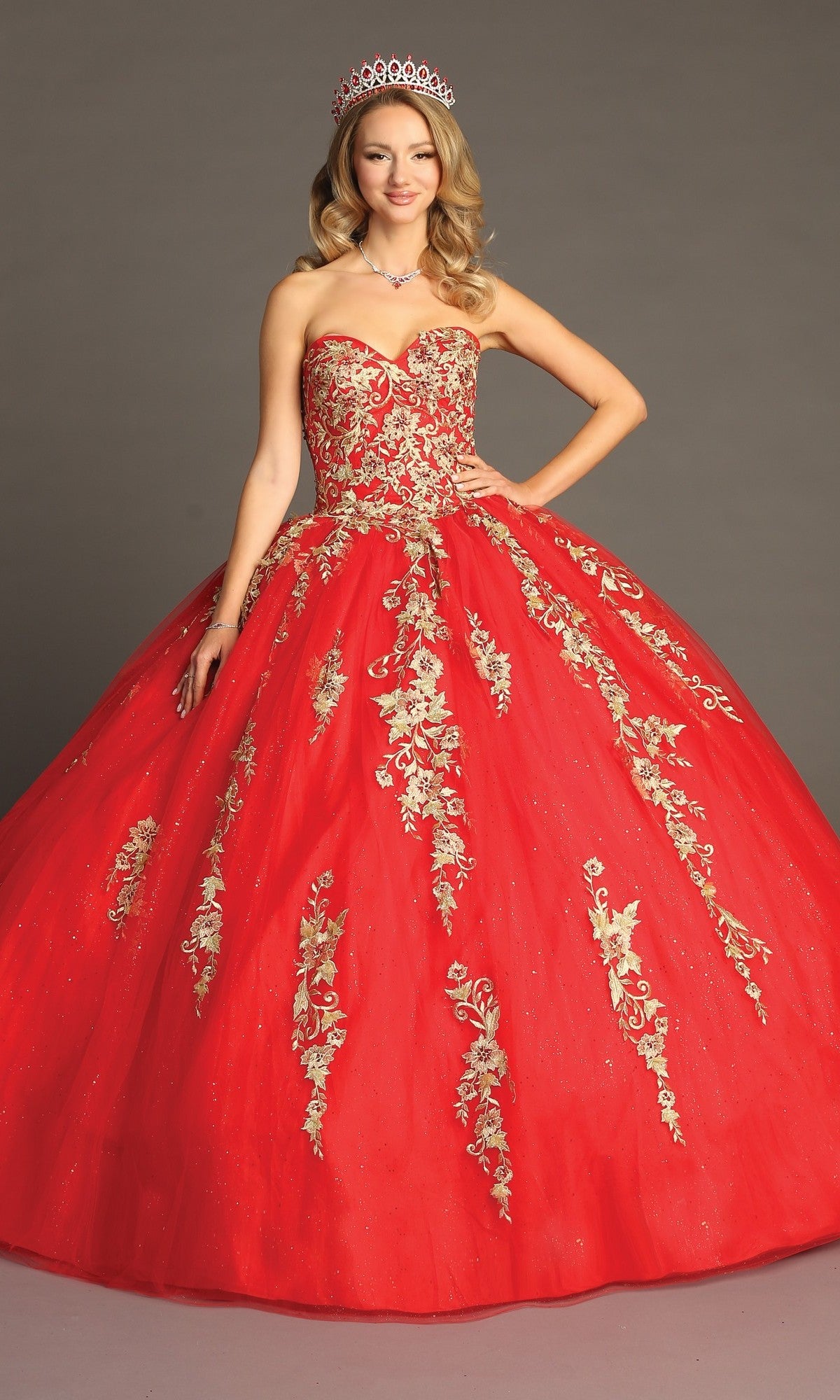 A woman stands against a plain backdrop wearing the Quinceanera Dress CHF3042 by Chicas, a strapless red and gold ballgown skirt adorned with exquisite floral embroidery. Paired with a tiara and necklace, this stunning dress exudes elegance and grace.