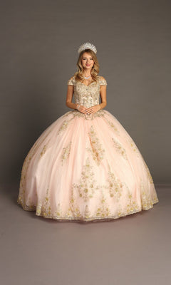 A young woman stands in a studio wearing the Quinceanera Dress CHF3051 by Chicas, an elegant pink gown adorned with gold embroidery and featuring a voluminous ballgown skirt; she clasps her hands gracefully in front of her as a sparkling tiara rests atop her head.