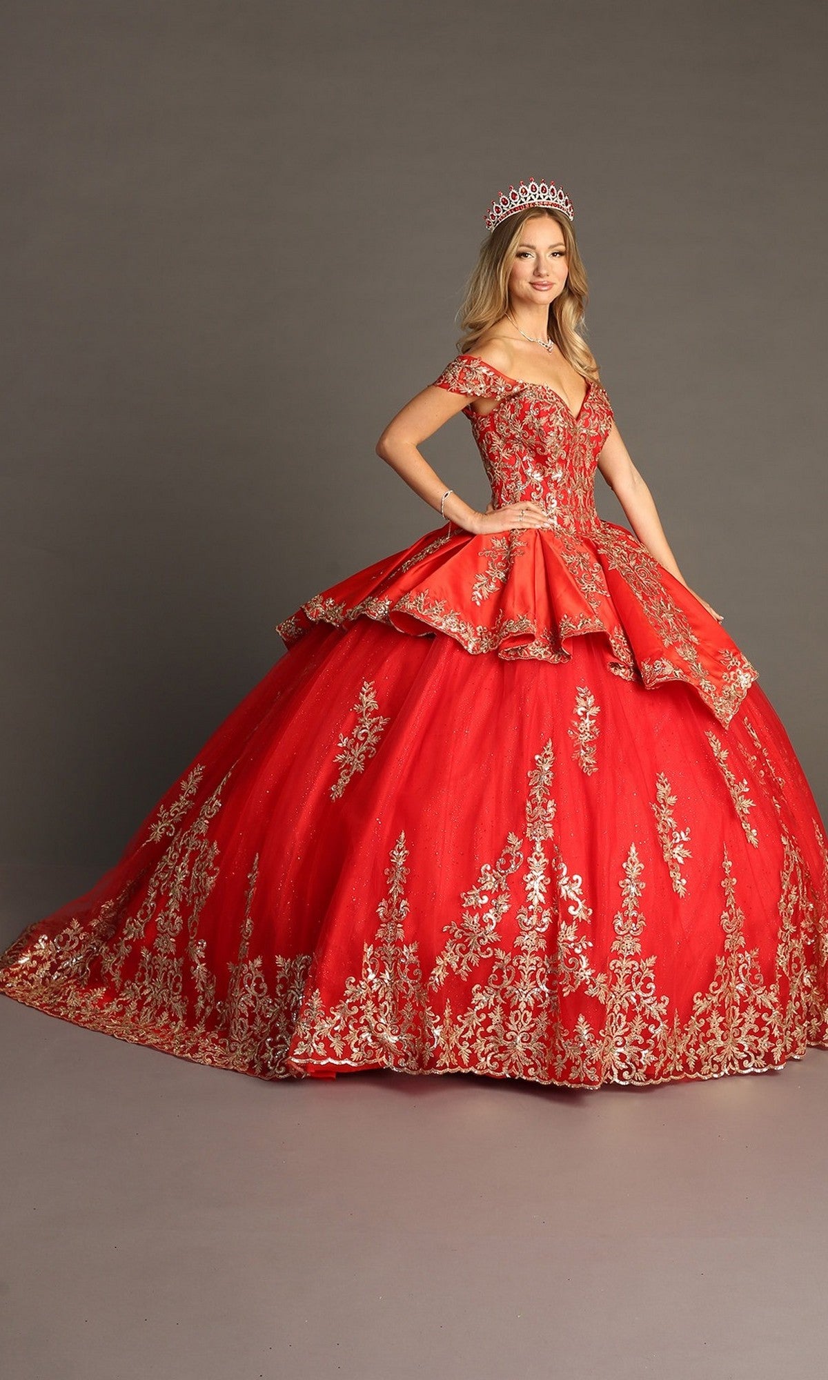 A woman models the Quinceanera Dress CHF3052 By Chicas—a stunning red gown with gold embroidery—paired with a matching tiara, posing against a plain gray background with her hands on her hips and looking at the camera.