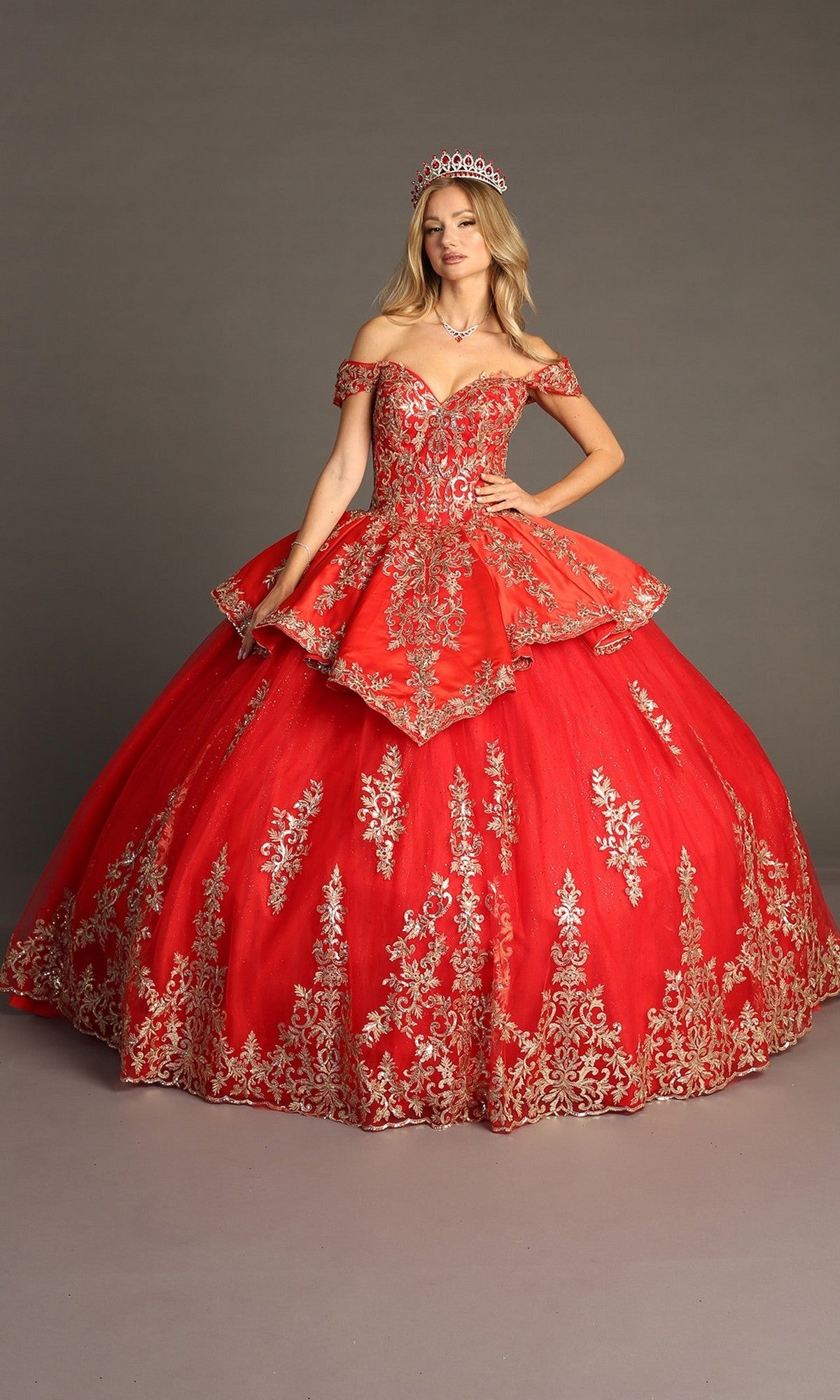A woman wearing the Quinceanera Dress CHF3052 By Chicas in Red/Gold with gold embroidery and a tiara, standing against a plain gray background.