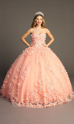 A young woman stands smiling with her hands on her hips against a plain gray background, wearing the Quinceanera Dress CHF3055 By Chicas. The strapless gown features 3D floral appliques and a glitter tulle ballgown skirt, and she completes the elegant look with a shimmering tiara.