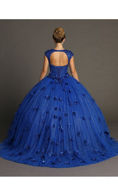 A person wearing the Quinceanera Dress CHF3068 By Chicas: a blue ball gown featuring cap sleeves, an open back, and a full tulle skirt adorned with 3D flowers and floral accents, standing against a plain background.