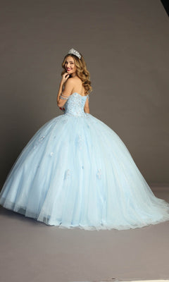 A woman wearing the Quinceanera Dress CHF3071 By Chicas, featuring a light blue hue and beaded bodice, stands on a gray backdrop with a sparkling tiara, looking over her shoulder and smiling.