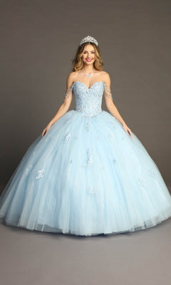 A woman poses against a plain studio backdrop wearing the Quinceanera Dress CHF3071 by Chicas—a light blue glitter-tulle ballgown featuring off-the-shoulder sleeves and a beaded bodice—styled with a tiara and necklace.