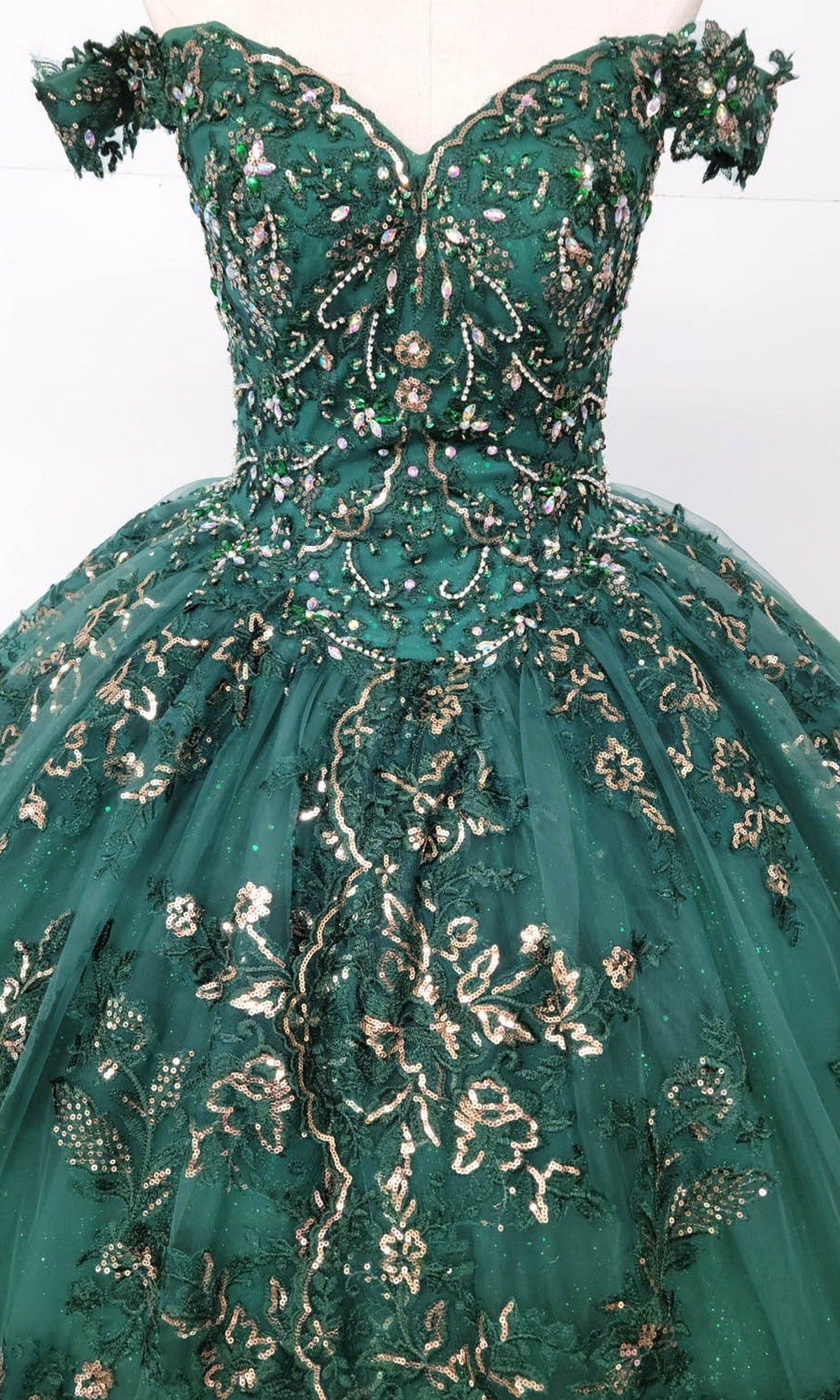 The Quinceanera Dress CHF3072 By Chicas is a green off-the-shoulder gown featuring a voluminous tulle ballgown skirt, adorned with delicate beading and intricate gold and silver metallic embroidery.