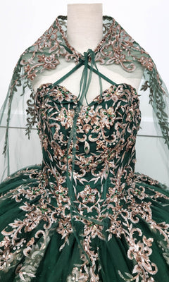 The Quinceanera Dress CHF3073 By Chicas is a strapless green ball gown adorned with gold and metallic-silver embroidery, complete with a matching sheer cape. Displayed on a dress form, this elegant gown features a glitter-tulle skirt that adds extra sparkle to its stunning design.