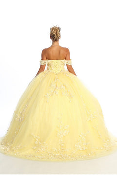 A person stands facing away, wearing the Quinceanera Dress CHF3074 By Chicas—a yellow off-shoulder ball gown featuring floral appliques and delicate lace embroidery—paired with a tiara, set against a plain white background.