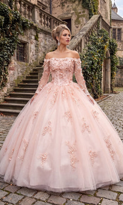 A woman in the Quinceanera Dress CHF3076 By Chicas, featuring an ornate off-the-shoulder design in blush, stands on a cobblestone path near stone stairs and an ivy-covered historic building.