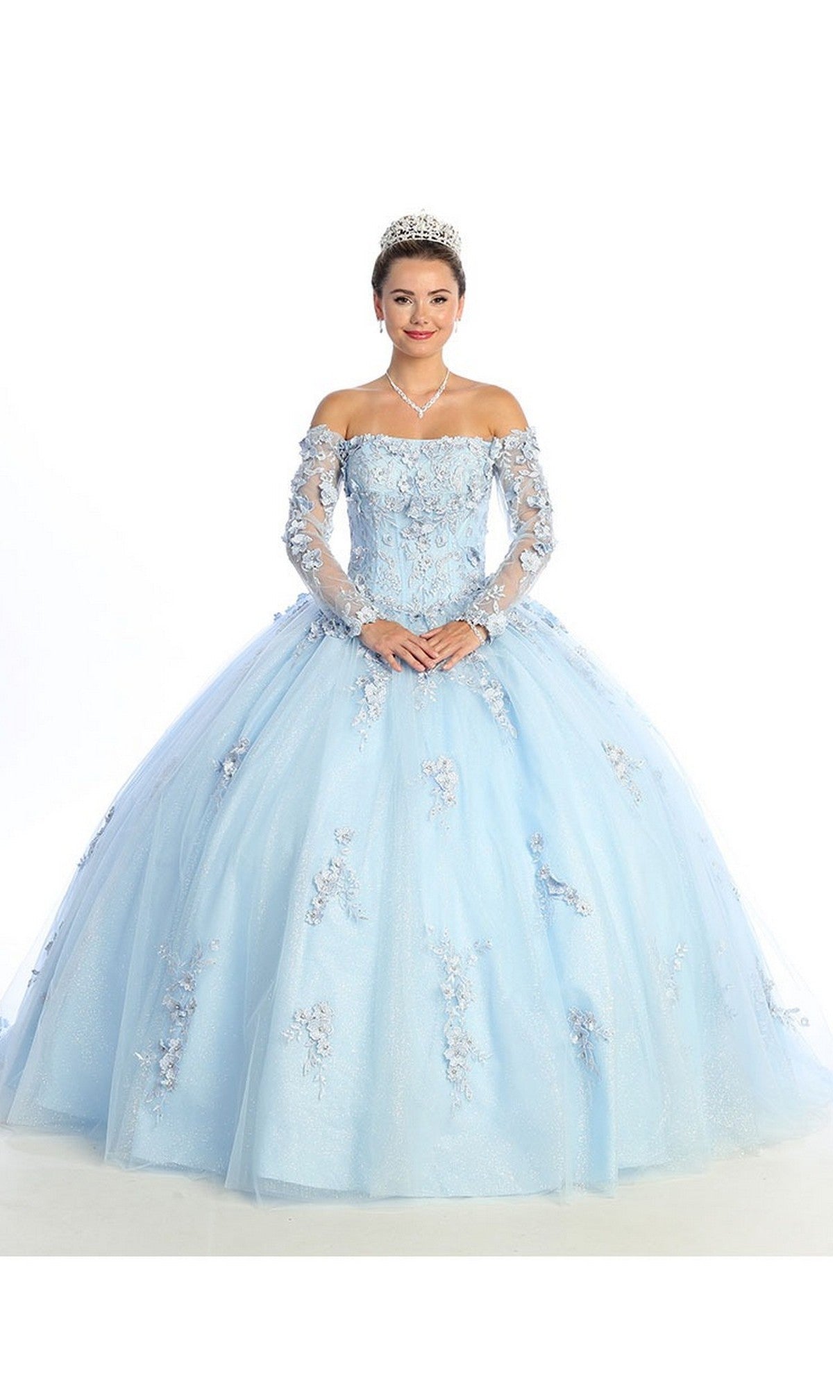 A person wearing the Quinceanera Dress CHF3076 By Chicas in sky blue, featuring an off-the-shoulder ballgown design with delicate floral details, accessorized with a sparkling tiara and necklace, stands against a plain white background. This elegant ensemble is perfect for any memorable quinceanera moment.