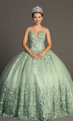 A young woman stands against a gray background, hands clasped in front and smiling softly, wearing the Quinceanera Dress CHF3077 By Chicas—a sparkling tulle ballgown adorned with delicate butterfly appliques and paired with a tiara.