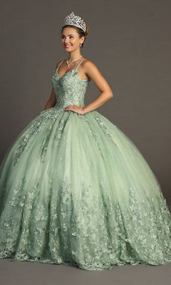 A woman wearing a tiara and the Quinceanera Dress CHF3077 By Chicas in sage stands against a plain backdrop, smiling slightly. The light green gown features floral detailing and delicate butterfly appliques, adding an enchanting touch to her elegant look.