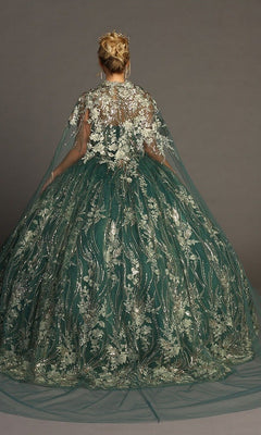 A woman stands facing away against a plain backdrop, wearing the Quinceanera Dress CHF3079 By Chicas—a strapless green ballgown adorned with metallic floral embroidery and paired with a sheer, embroidered cape.