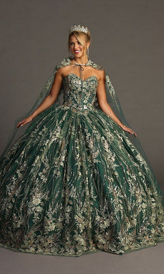 A woman stands against a plain background, smiling with arms slightly raised, her jeweled crown catching the light as she wears the Quinceanera Dress CHF3079 By Chicas—a strapless green ballgown adorned with metallic floral embroidery and a sheer, embroidered cape.