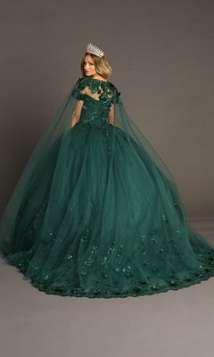 A woman wearing the Quinceanera Dress CHF3082 By Chicas—a dark green gown adorned with sequin details, a sheer cape, and a silver crown—stands on a plain backdrop, facing slightly away from the camera. The dress features delicate 3D floral appliques that add an elegant touch to her ensemble.