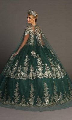 A woman stands gracefully against a plain backdrop, elegantly crowned and dressed in the enchanting Quinceanera Dress CHF3083 By Chicas—a large green ballgown adorned with glitter tulle and silver floral embroidery—capturing the regal essence of a traditional Quinceañera celebration.