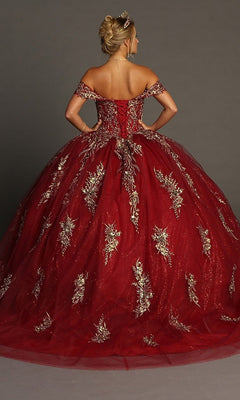 A woman stands with her hands on her hips, facing away from the camera against a plain background, wearing the Quinceanera Dress CHF3084 By Chicas—a stunning off-the-shoulder ballgown featuring gold floral embroidery and glitter tulle.