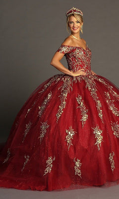 A woman wearing the Quinceanera Dress CHF3084 By Chicas—an ornate red off-the-shoulder gown decorated with gold floral embroidery and paired with a matching crown—stands against a plain gray background.