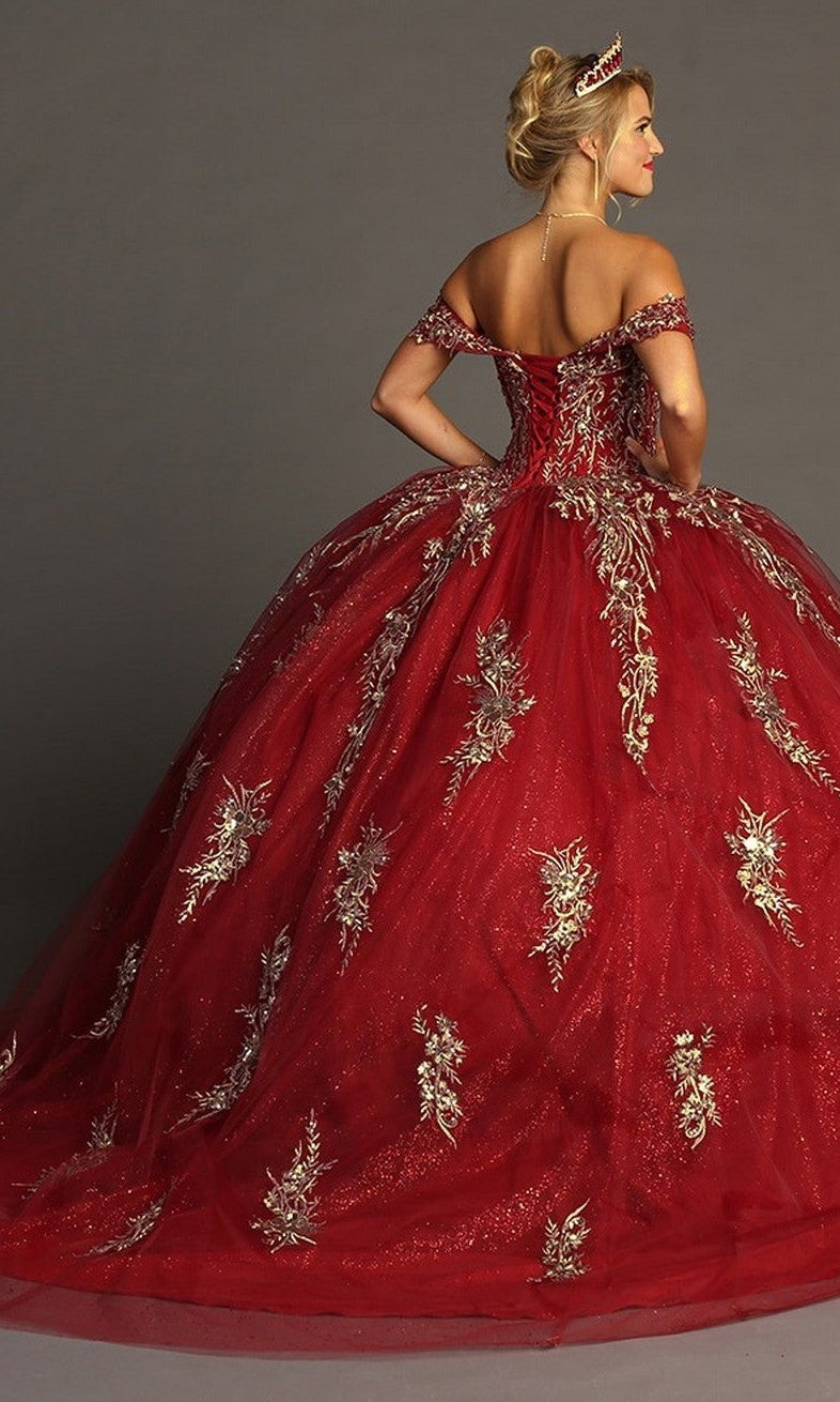 A woman wears the Quinceanera Dress CHF3084 By Chicas—a striking red, off-the-shoulder gown adorned with gold floral embroidery—paired with a delicate tiara, standing with her back to the camera against a plain background.
