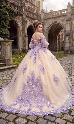 A woman wearing the Quinceanera Dress CHF3087 By Chicas—an elegant off-the-shoulder gown adorned with purple 3D floral appliqués—stands on a cobblestone path, her back to a stone building decorated with arches.