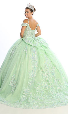 A woman wears the Quinceanera Dress CHF3089 by Chicas—a light green, off-shoulder ball gown with a glitter-tulle skirt and delicate floral lace details on the corset bodice. She accessorizes with a tiara and glances back over her shoulder against a plain white background.