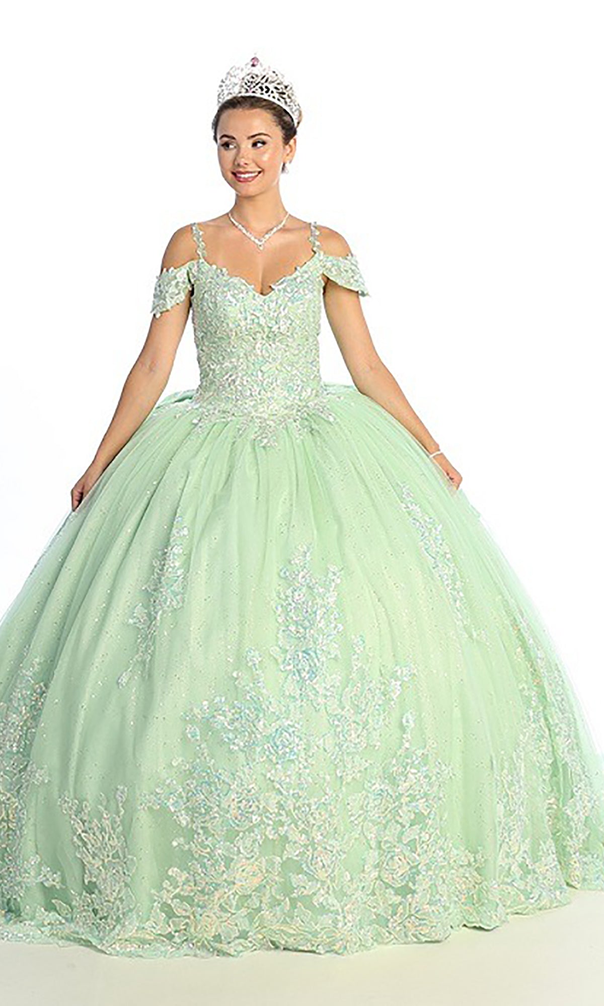 A woman wearing the Quinceanera Dress CHF3089 by Chicas—a light green, off-the-shoulder ball gown featuring a floral lace corset bodice—paired with a tiara and necklace, stands against a plain white background.