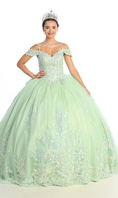 A young woman wearing the Quinceanera Dress CHF3089 By Chicas, a light green glitter-tulle ballgown featuring off-the-shoulder sleeves and a floral lace corset bodice, accessorized with a tiara and necklace, stands against a plain white background.