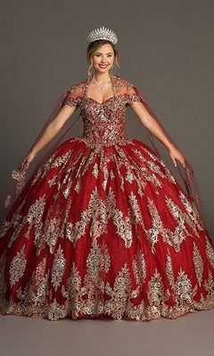 A woman dressed in the Quinceanera Dress CHF3090 By Chicas in burgundy and gold with glitter tulle and gold embroidery, accessorized with a silver tiara and jewelry, stands against a plain background.