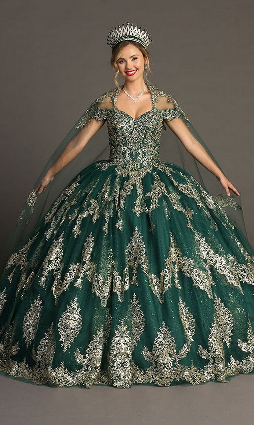 A woman is wearing the Quinceanera Dress CHF3090 By Chicas in a striking green and gold color, featuring ornate gold embroidery, a jeweled tiara, necklace, and a sheer cape with layers of glitter tulle, standing against a neutral background.