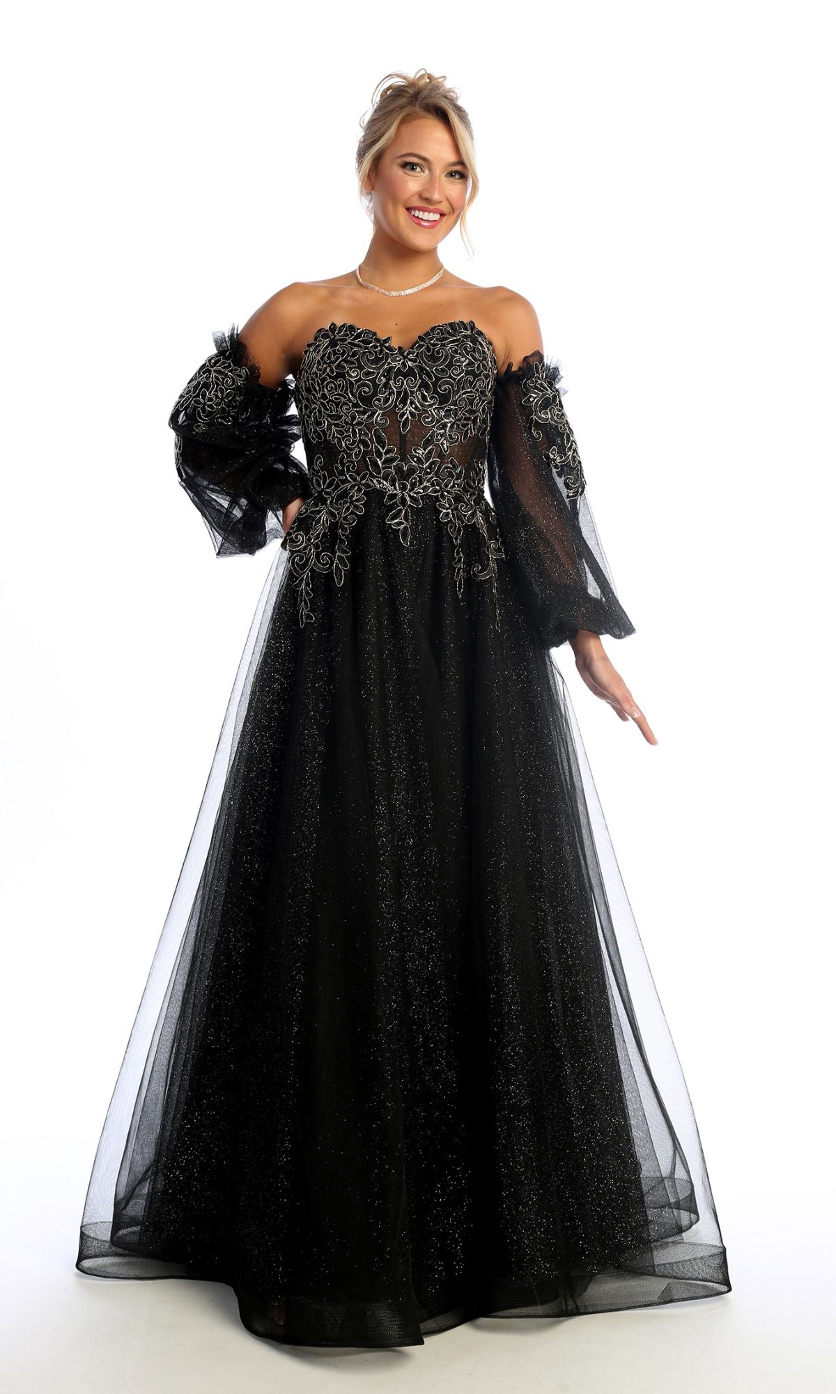 A woman wearing the Chicas CHF3093 Long Sleeve Long A-Line Prom Dress stands against a white background, smiling. The black formal gown features silver embroidery and sheer, puffy sleeves for an elegant look.