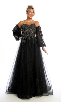 A woman wearing the Chicas CHF3093 Long Sleeve Long A-Line Prom Dress stands against a white background, smiling. The black formal gown features silver embroidery and sheer, puffy sleeves for an elegant look.