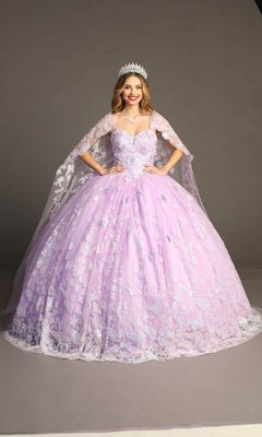 A woman stands in the Quinceanera Dress CHF3097 By Chicas, a lilac gown adorned with floral details and delicate butterfly appliques. She wears a tiara and a sheer glitter tulle cape, posing with hands on hips against a plain gray background.