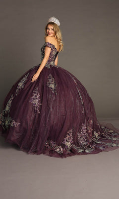 A woman is posing against a plain background, wearing the Quinceanera Dress CHF3099 by Chicas—an off-the-shoulder, burgundy gown adorned with intricate floral embroidery and featuring a dramatic ballgown skirt with a long train. She completes the regal look with a silver crown on her head.