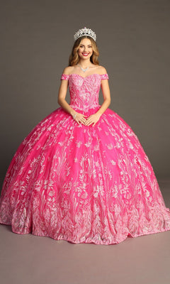 A young woman stands against a plain backdrop, smiling at the camera in the Quinceanera Dress CHF3100 By Chicas—a bright pink, off-the-shoulder gown featuring delicate floral patterns and a flowing tulle ballgown skirt. She completes her look with a jeweled tiara and necklace.
