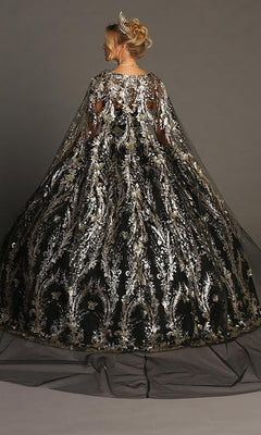 A woman in a silver tiara wears the Quinceanera Dress CHF3101 By Chicas—an off-the-shoulder black ball gown adorned with silver floral embroidery and metallic-silver embellishments, featuring a sheer, matching cape and a dramatic tulle skirt. She stands against a gray background.