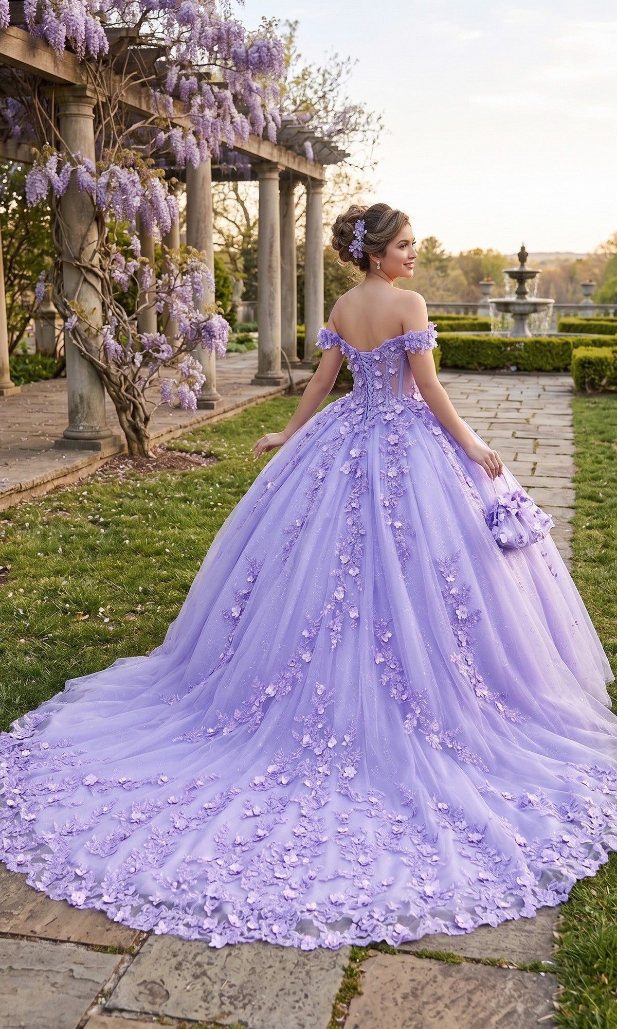 Wearing the Quinceanera Dress CHF3102 By Chicas, a woman stands on a stone path in a garden, her back to the camera. The gown features an off-the-shoulder neckline, a tulle ballgown skirt, and intricate 3D floral appliques.