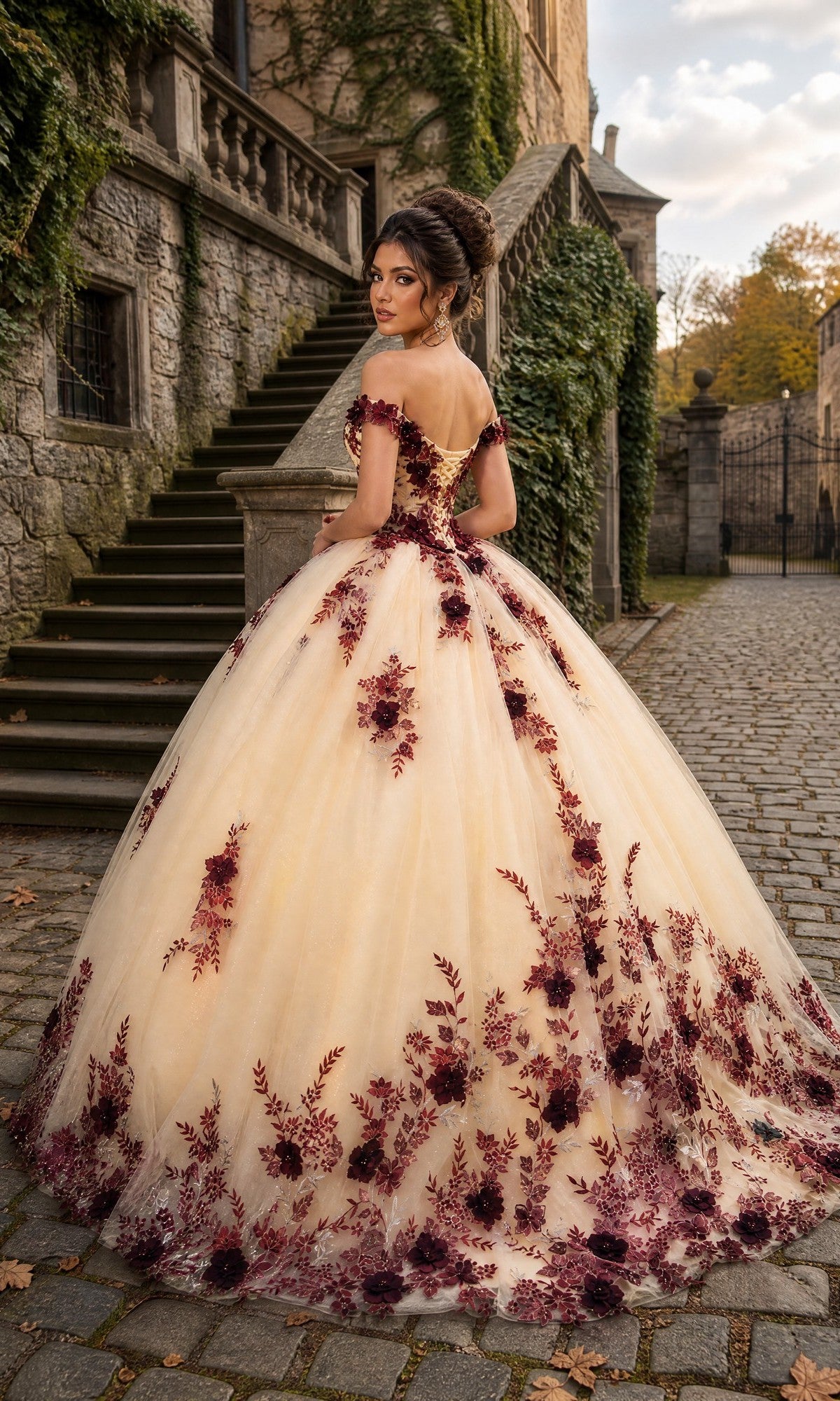 A woman wearing the Quinceanera Dress CHF3111 By Chicas, an ornate off-the-shoulder ballgown adorned with red floral embroidery and delicate 3D flower accents, stands on a cobblestone path near stone stairs and ivy-covered walls, looking over her shoulder.