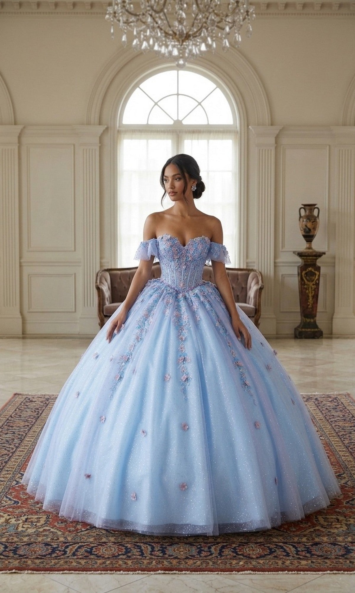 A woman stands indoors wearing the Quinceanera Dress CHF3114 By Chicas, a light blue, off-the-shoulder gown featuring delicate 3D floral appliques and a voluminous tulle skirt.