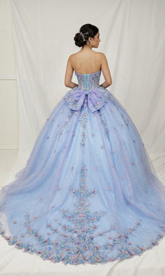 A woman wearing the Quinceanera Dress CHF3114 By Chicas—a strapless lavender ball gown accented with 3D floral appliques and a large bow—stands with her back to the camera against a plain white backdrop.